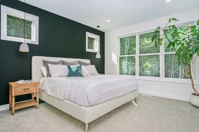 A pale bed stands against a deep green wall beside timber bedside tables.