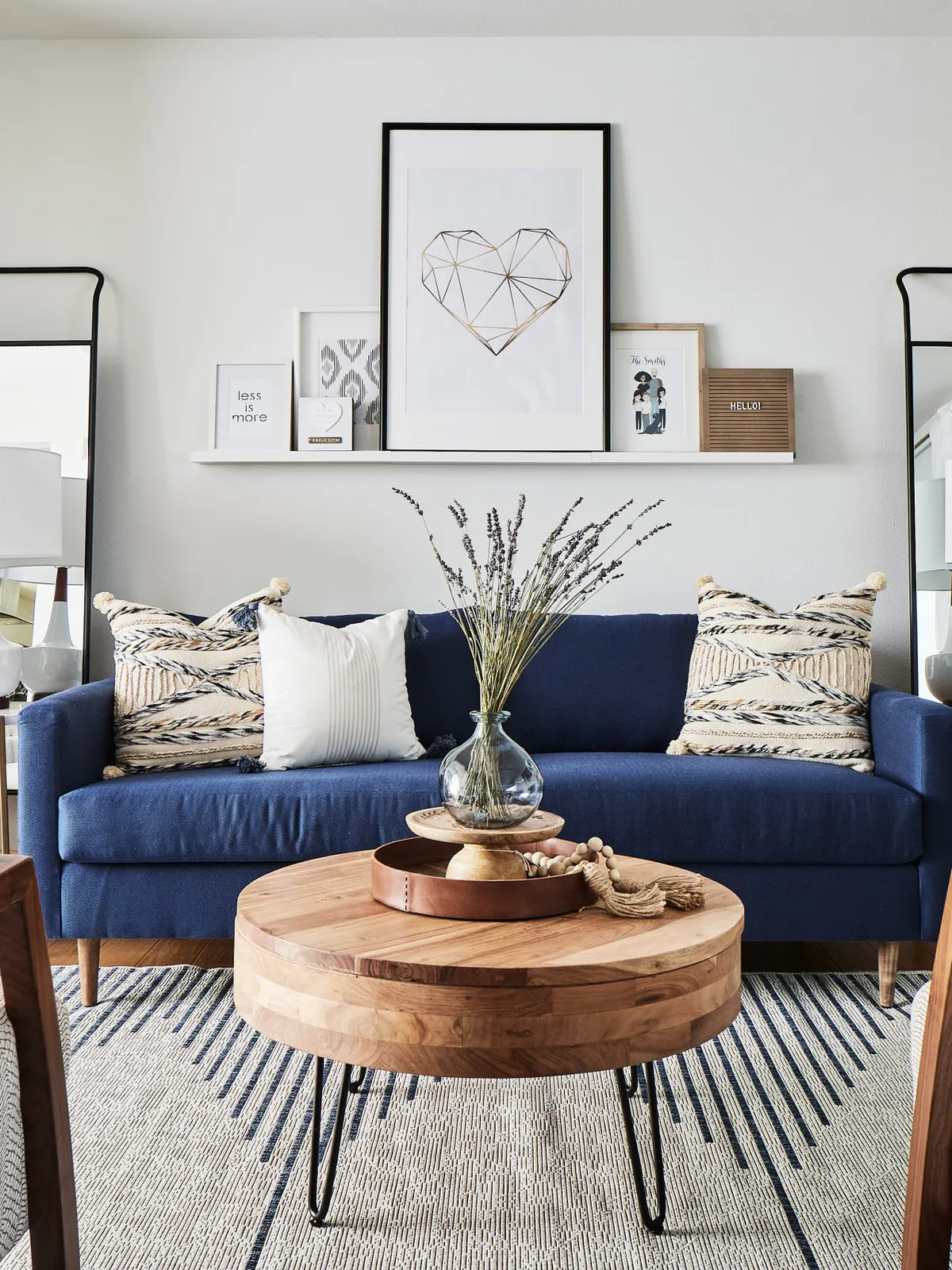 A round timber coffee table sits in front of a blue sofa and pale wall art.