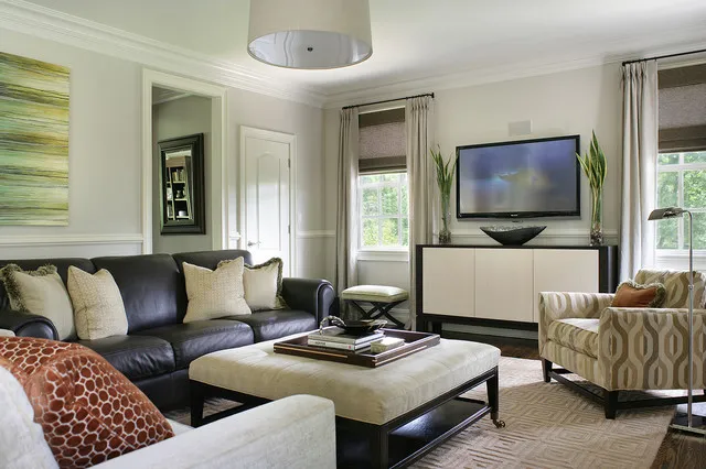 A dark leather sofa sits beside pale walls, a light ottoman and patterned chairs.
