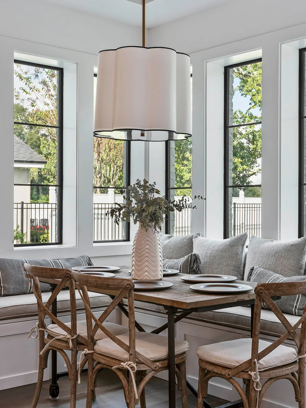 Timber chairs with pale cushions surround a table beside broad windows and a large shade.