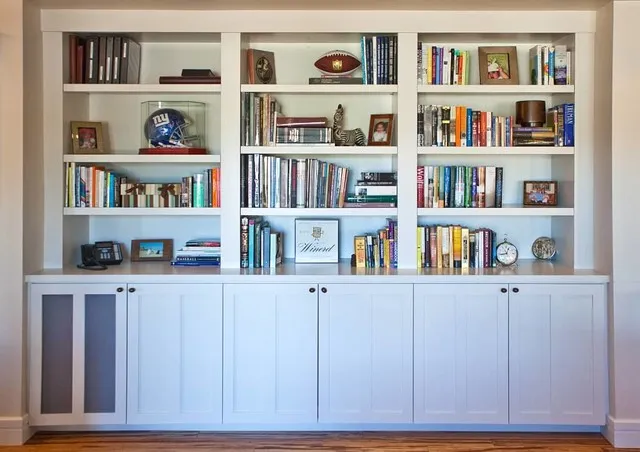 Pale blue lower cupboards sit beneath bookshelves filled with framed pieces and objects.