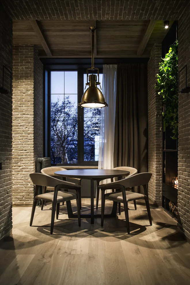 A round dark table and chairs sit beneath a pendant in a brick-lined dining nook