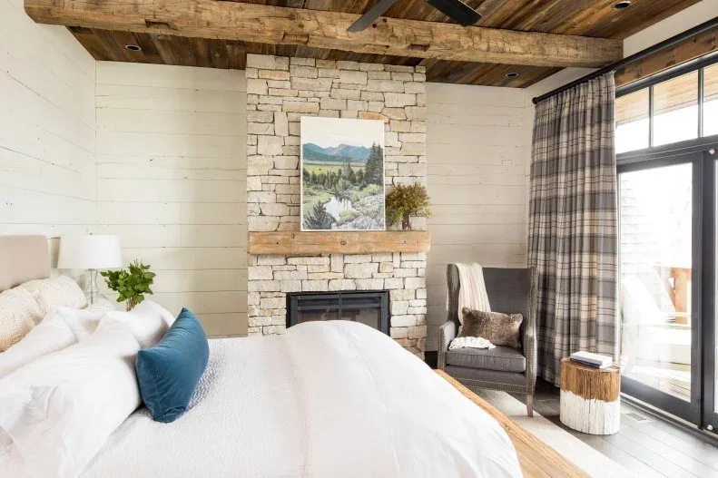 Rustic bedroom with pale fireplace wall, wood ceiling, checked curtains and white bedding