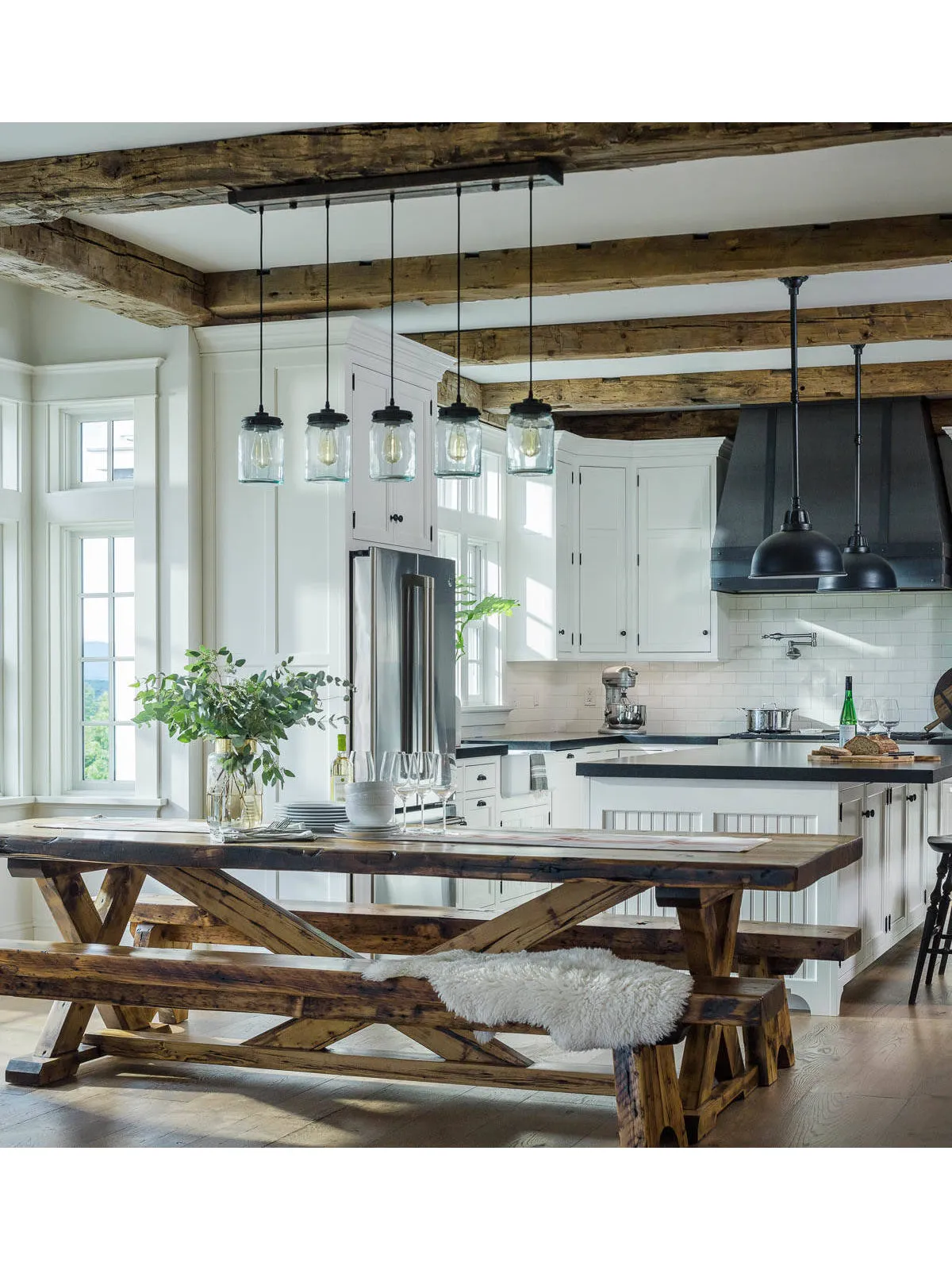 A timber table with benches sits beside a pale farmhouse kitchen under exposed beams.
