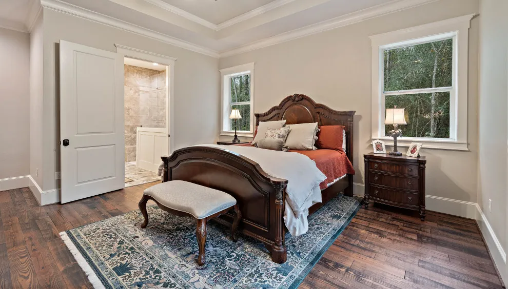 A dark timber bed stands on a varied reddish-brown floor beside pale walls