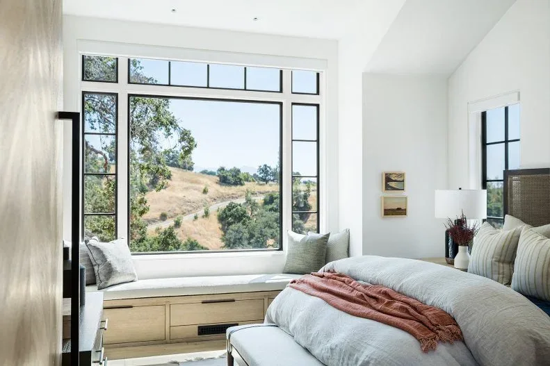 White bedroom with broad black-trimmed window, fitted pale wood window seat and soft bedding