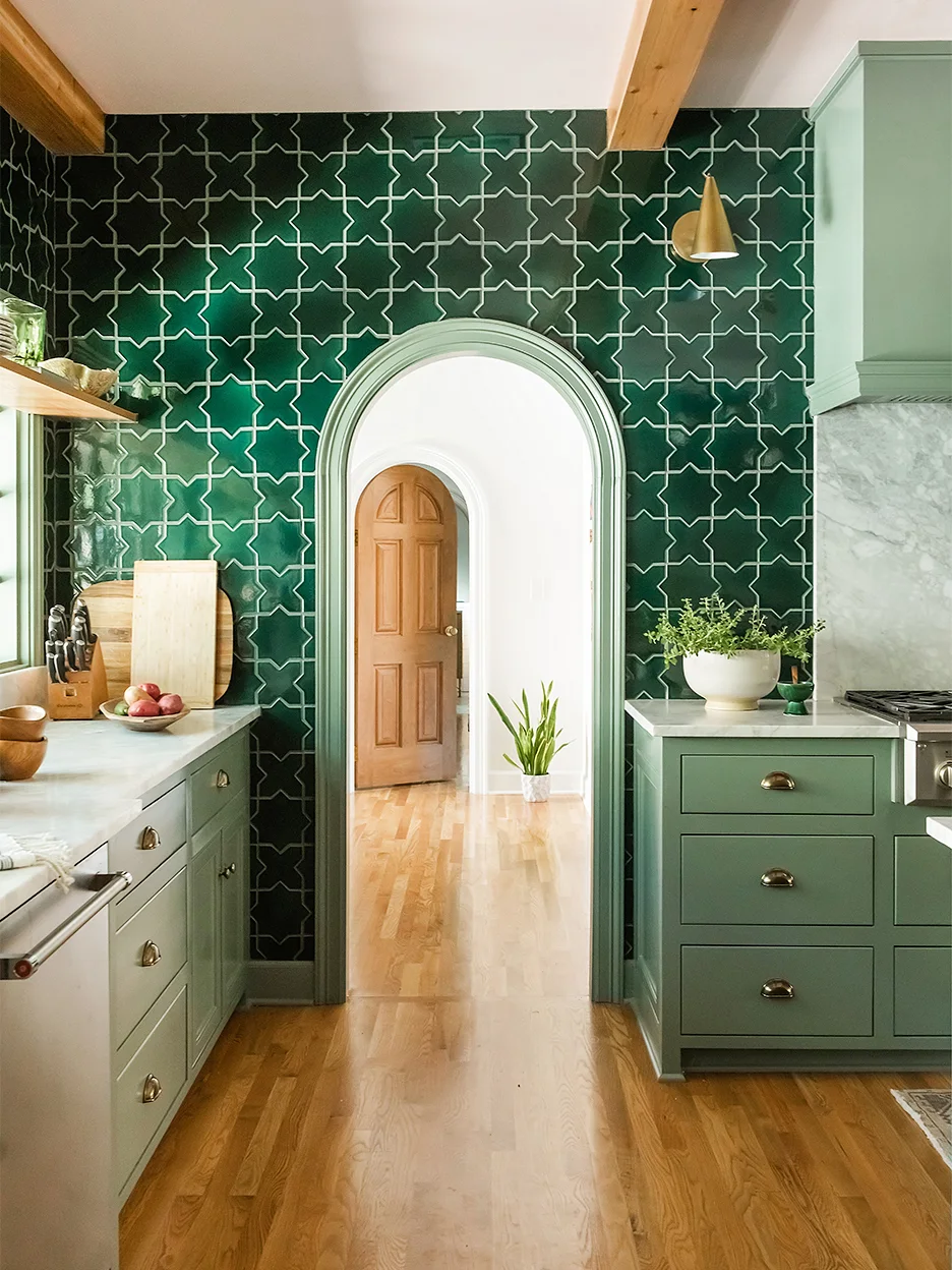 Deep green geometric wall tiles surround a pale-trimmed arched opening between green lower cupboards and light counters
