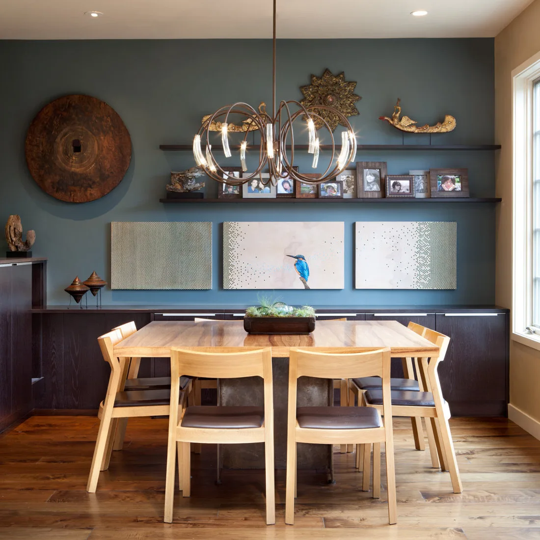 Two dark picture ledges with framed photographs above three artworks on a blue dining wall