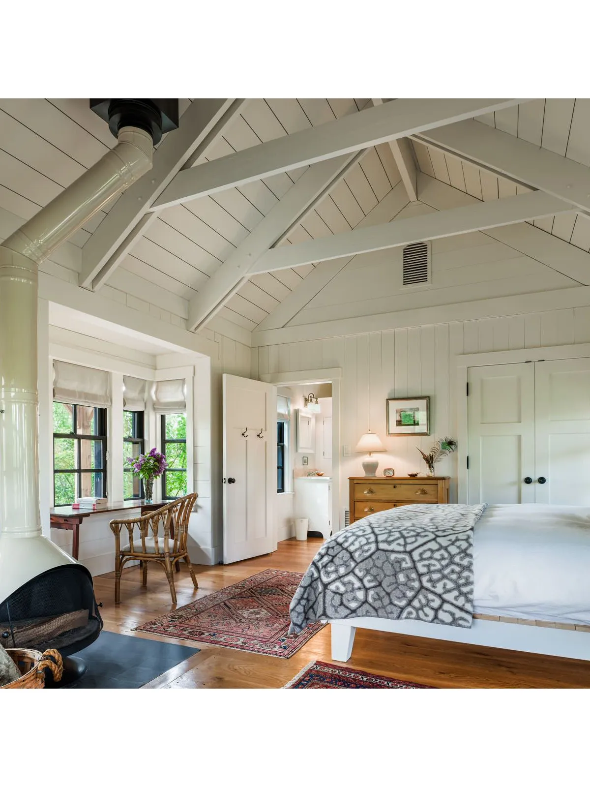 A broad pale timber ceiling spans a bedroom with a patterned coverlet and wood furniture.
