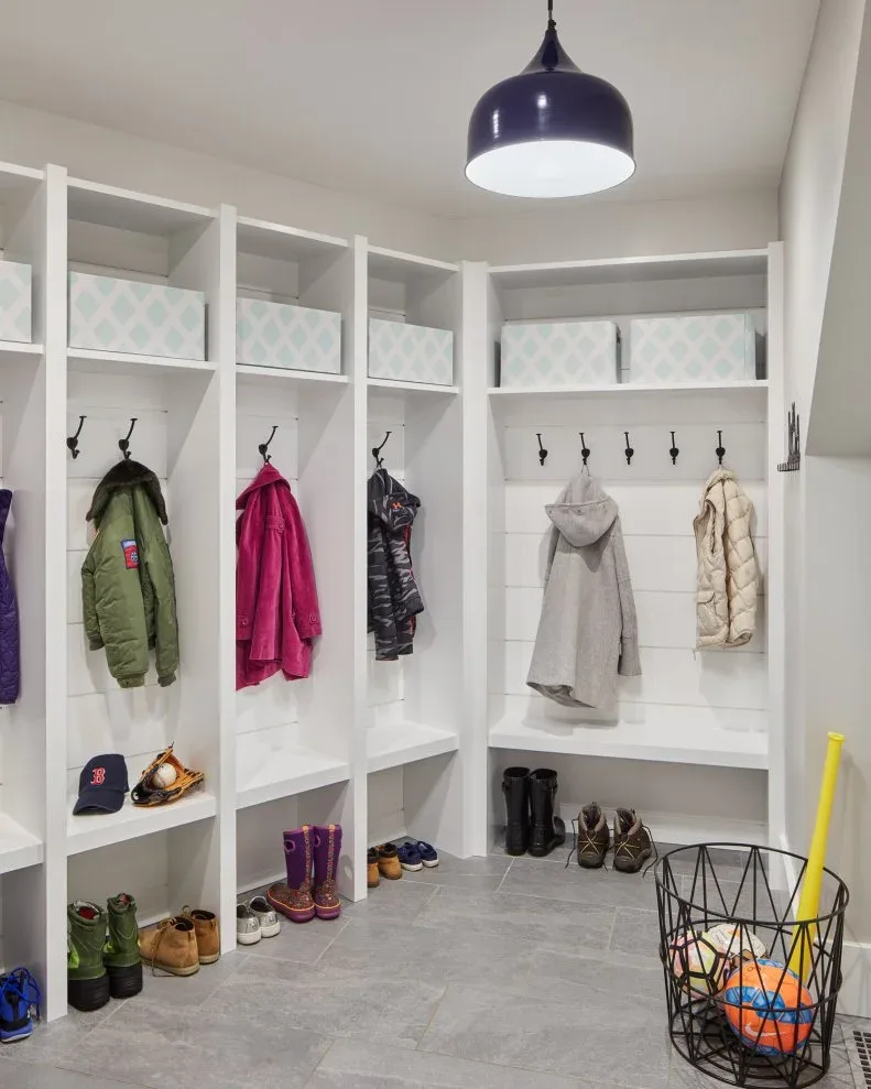 White corner mudroom coat bays with bench, upper patterned boxes, blue pendant and black wire basket holding balls