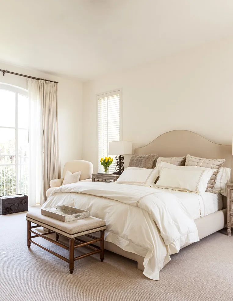 A curved beige headboard frames pale bedding beside a slim timber bench