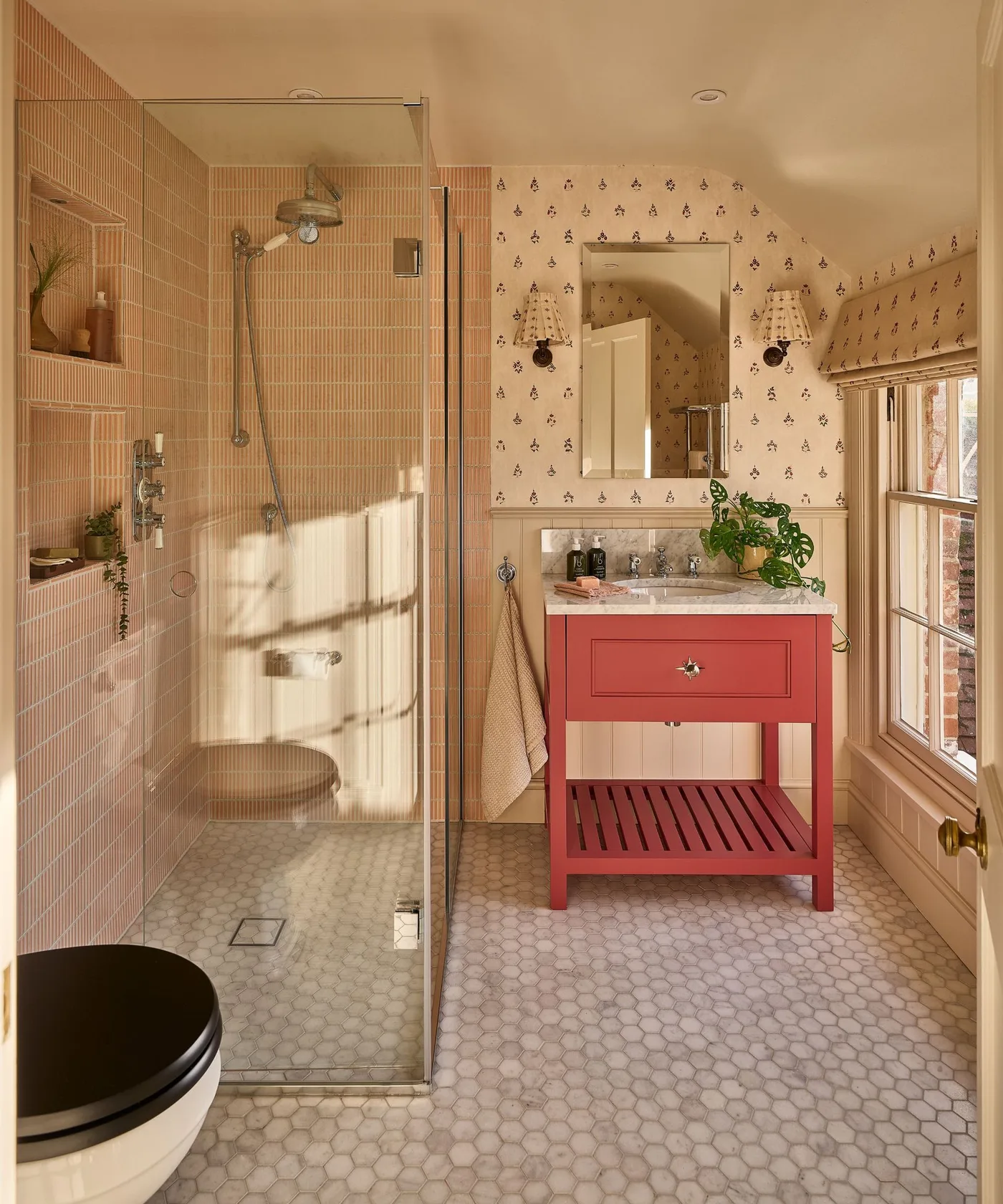 Warm-toned bathroom with tiny floral wallpaper above pale panels, coral vanity and enclosed shower