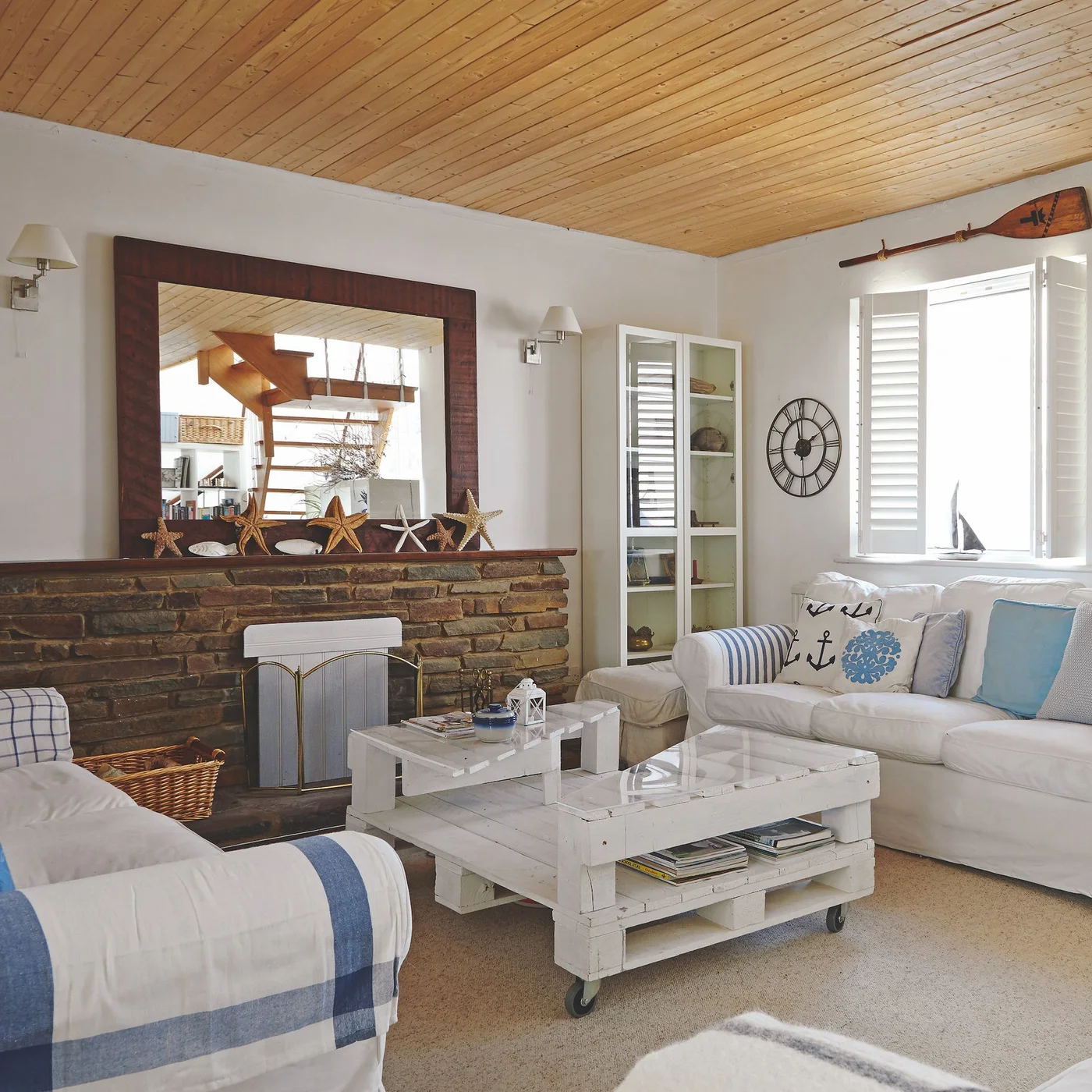 A textured brown fireplace wall sits beneath a wooden ceiling beside white sofas and a pale wheeled table