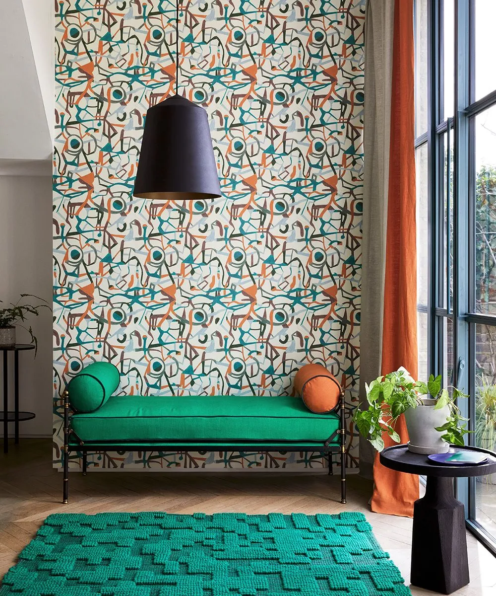 An intricate illustrated wall stands behind a green bench and warm cushions.