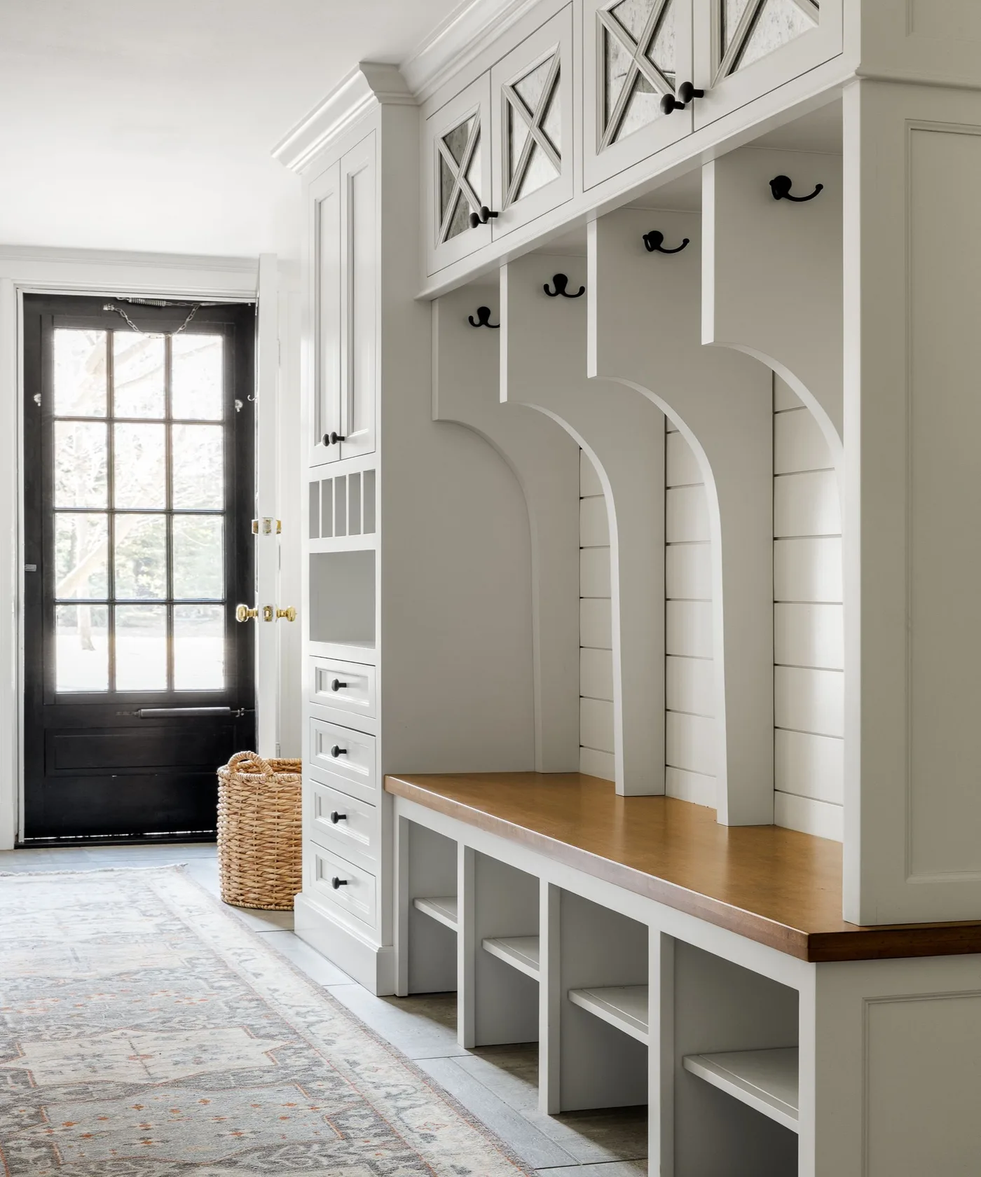 White entry storage with divided hook bays, wood bench, lower shoe spaces, upper X-detail doors and a narrow drawer unit