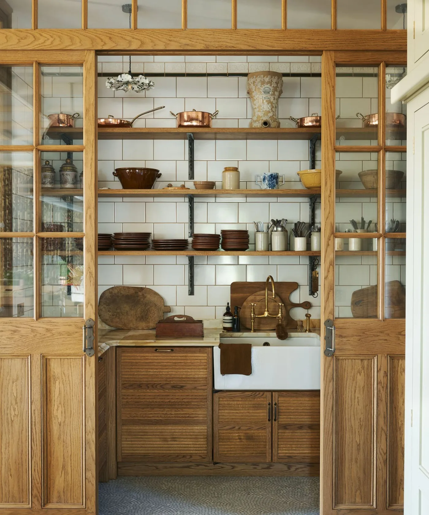 Wood-framed glazed pantry with pale tiled background, open shelves, serving pieces and farmhouse-style sink