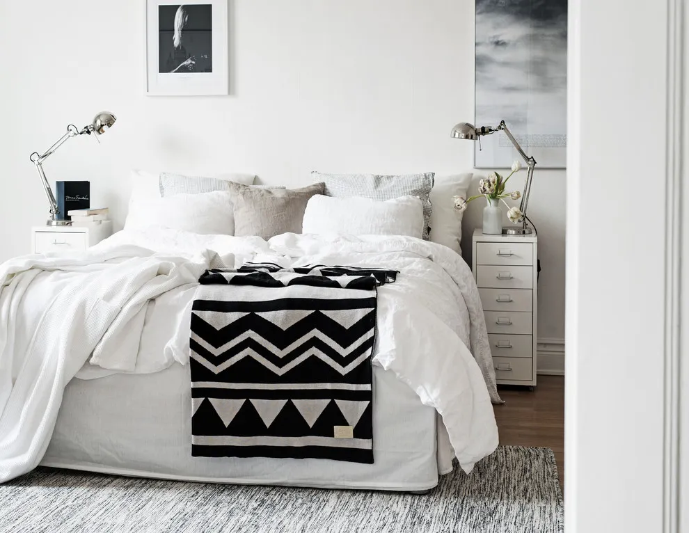 A black-and-white chevron textile lies over a pale bed in a bright room