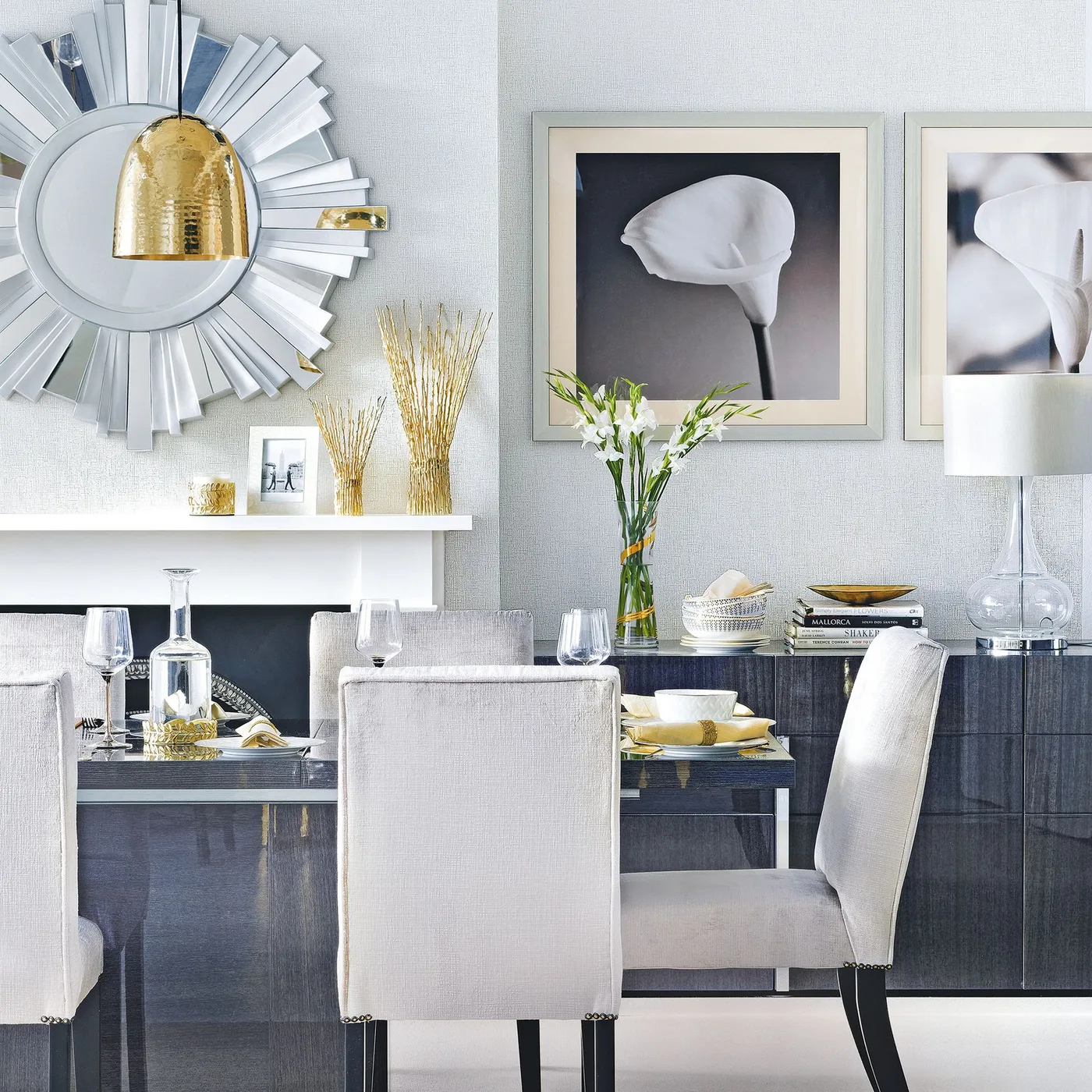 Silver sunburst mirror above a white fireplace beside a dark dining table with pale upholstered chairs