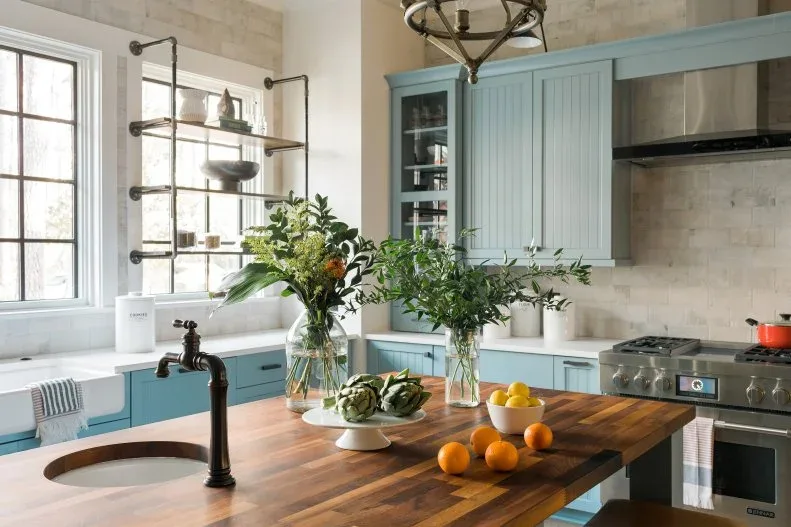 Blue paneled kitchen cabinets with wood island top, pale wall tile, open shelving and a black island faucet