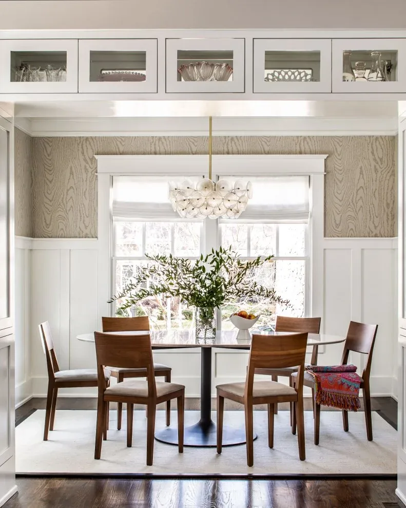 White dining wall panels beneath a wood-grain-patterned upper wall around a window and glass table