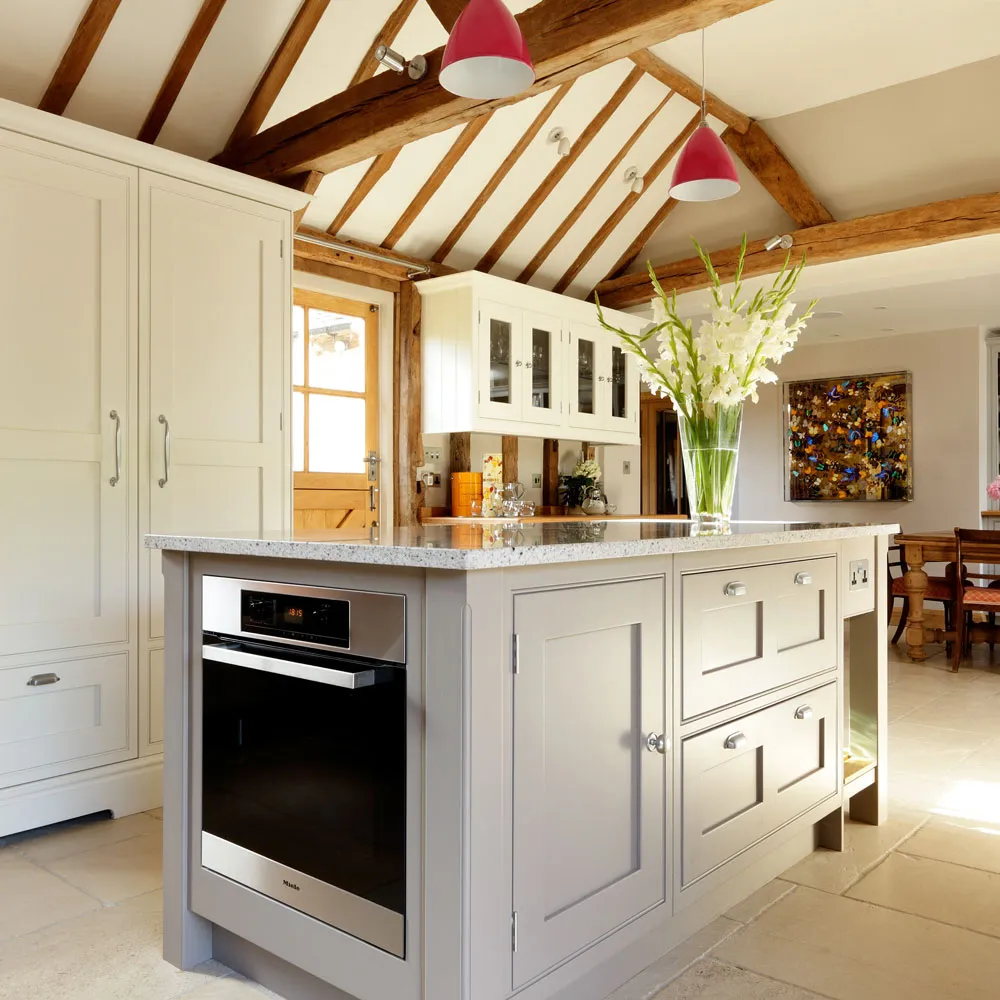 Cream perimeter cabinets surround a gray island beneath exposed wooden roof beams and red pendants