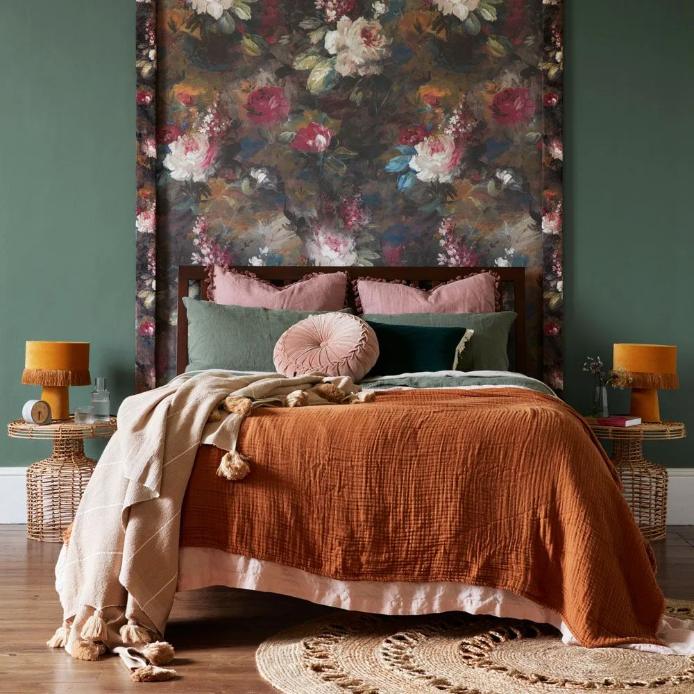 Large pale and pink flowers on a dark feature wall behind a bed between green painted walls.