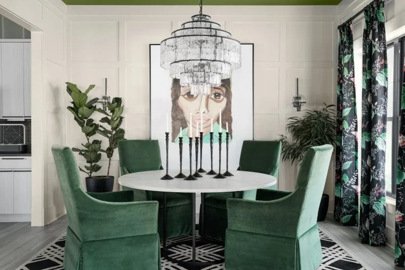 Cluster of slender black candlesticks with pale and green candles on a white round table surrounded by green chairs