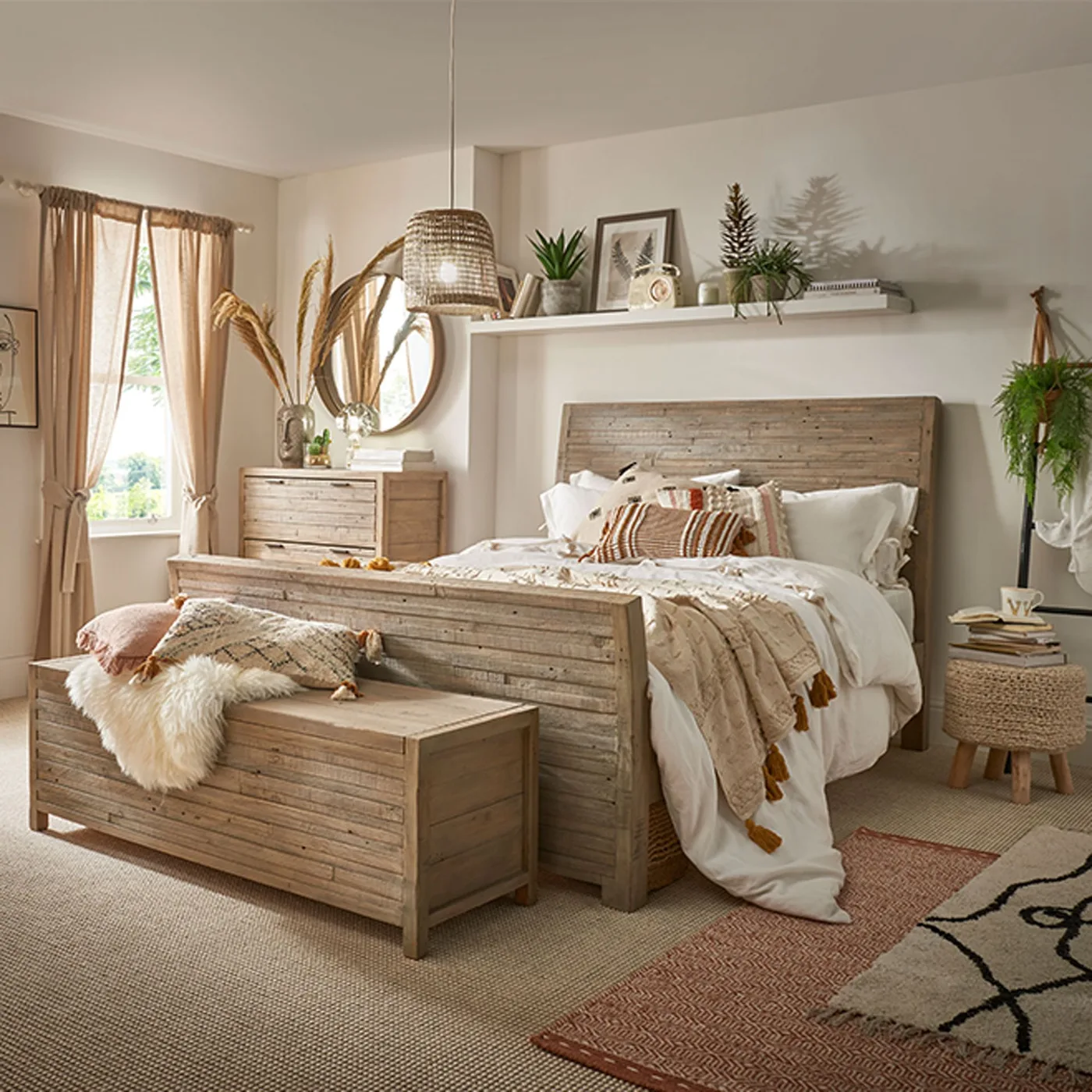 Neutral bedroom with wooden bed, matching chest and blanket box, white bedding, plants on a long shelf, hanging planter and woven ceiling shade.