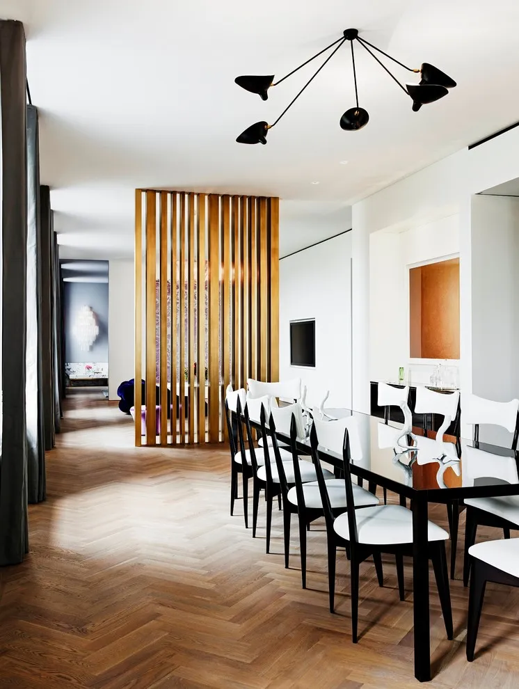 A long dining table sits beside a timber slat divider in an apartment
