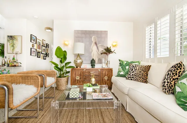 A pale sofa sits beside woven furniture, leafy plants and a textured-front cabinet.