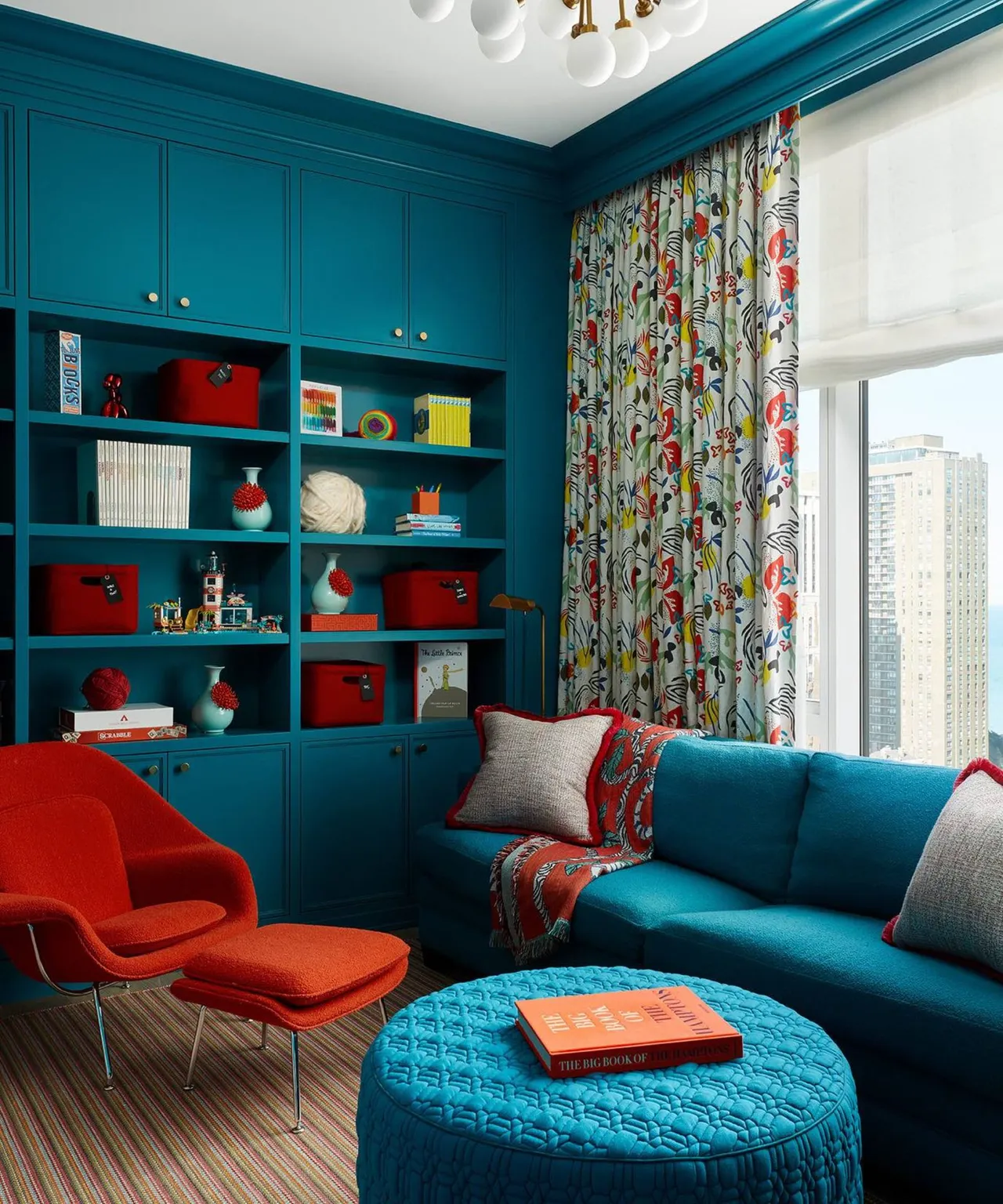 A teal sofa and matching shelves sit beside a red chair and patterned curtains.