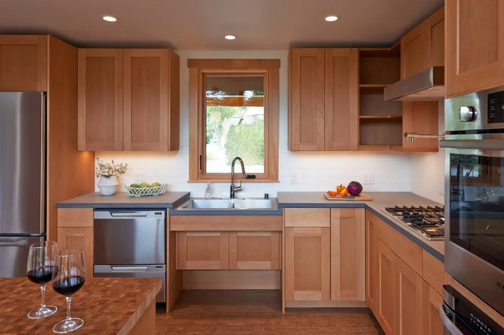 Warm wood cabinets frame a small kitchen with a sink window and a short counter return