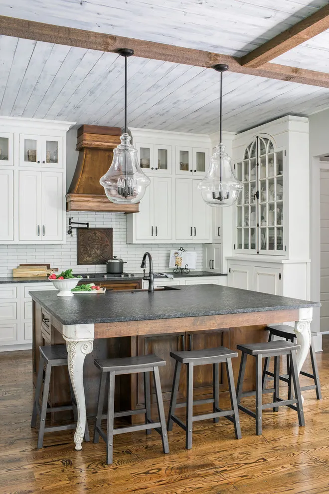 White cabinets surround a timber hood and dark island beneath exposed ceiling boards