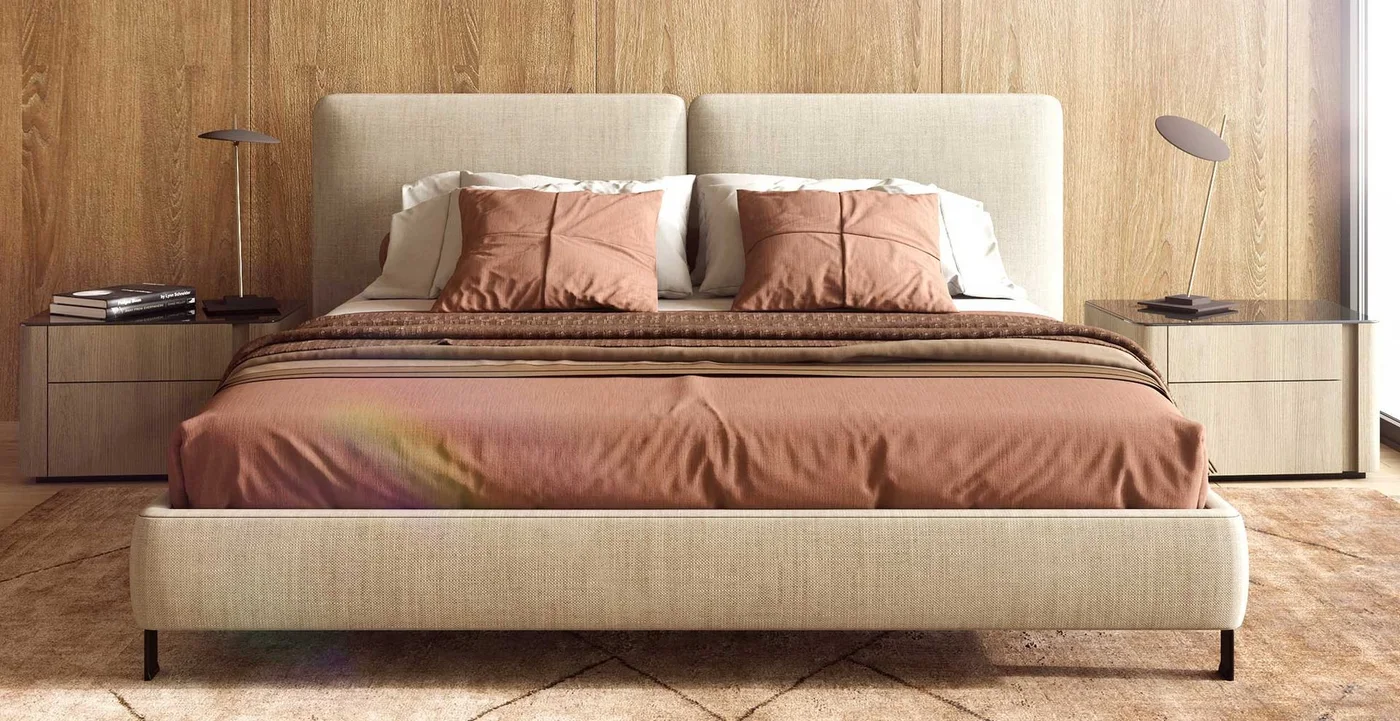 A pale upholstered bed with rust-colored bedding sits before wooden wall panels beside two drawer cabinets and slim lamps