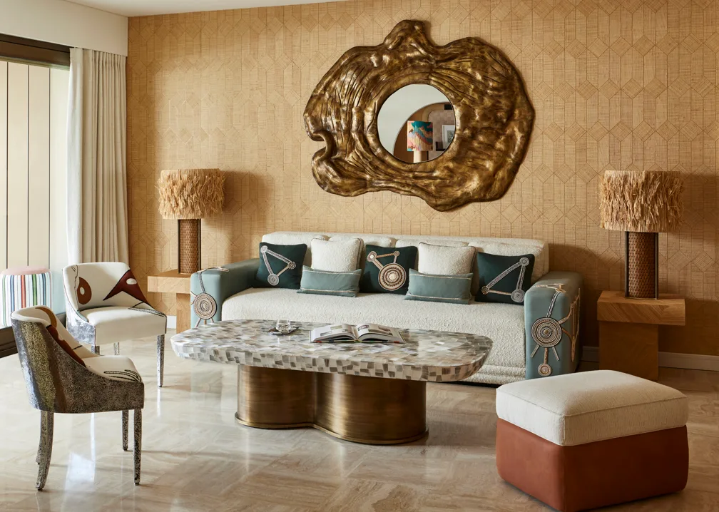 Ochre patterned living room wall behind pale seating, a sculptural gold-toned mirror and textured lamps