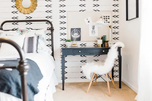 A dark compact desk sits beside a white textured chair against a patterned wall.