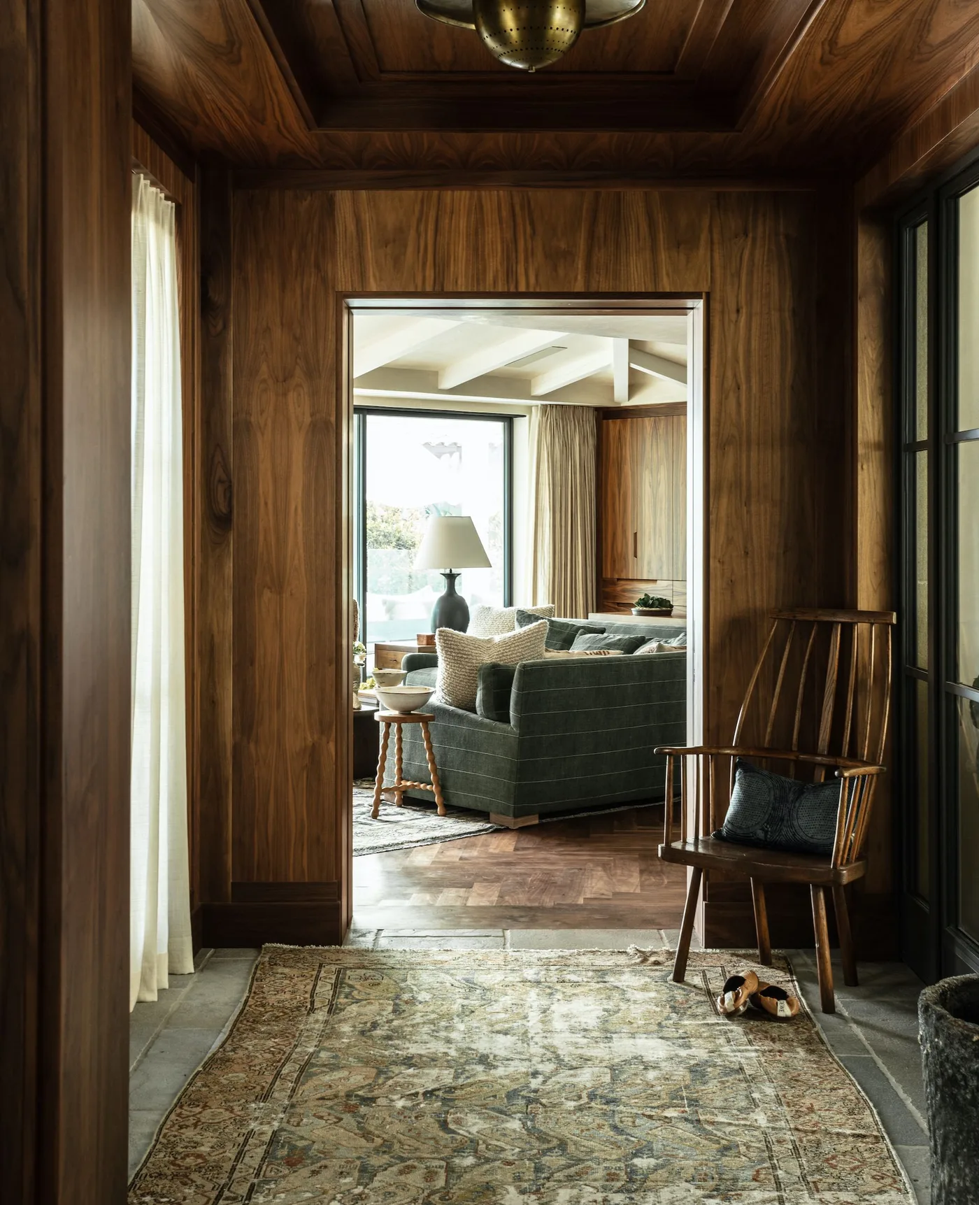 Muted patterned rug in a dark timber-lined entry with a spindle chair, glazed exterior door and adjoining living room