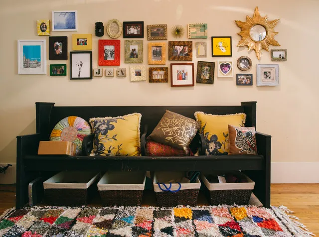 A black bench with colorful patterned cushions sits beneath a varied collection of framed pictures.
