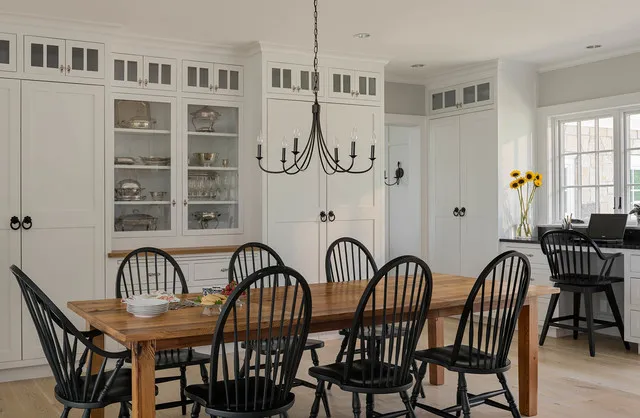 Black spindle chairs surround a timber dining table beside pale cupboards.