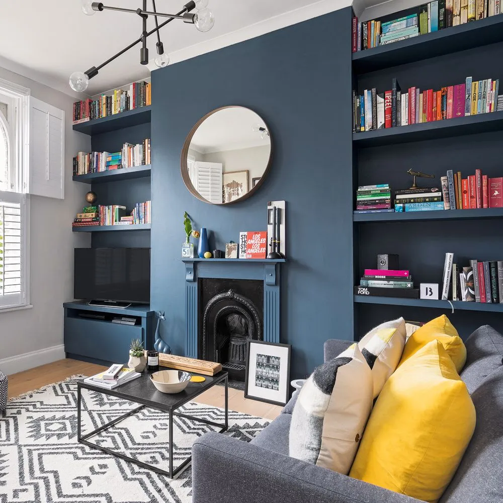 Navy alcove bookshelves and low television cabinet around matching fireplace wall and round mirror