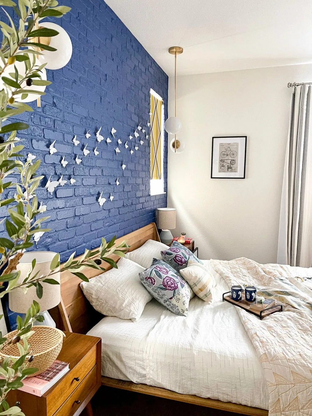 Deep blue painted brick bedroom wall with butterfly decorations, a wooden headboard, white bedding, and hanging lights.