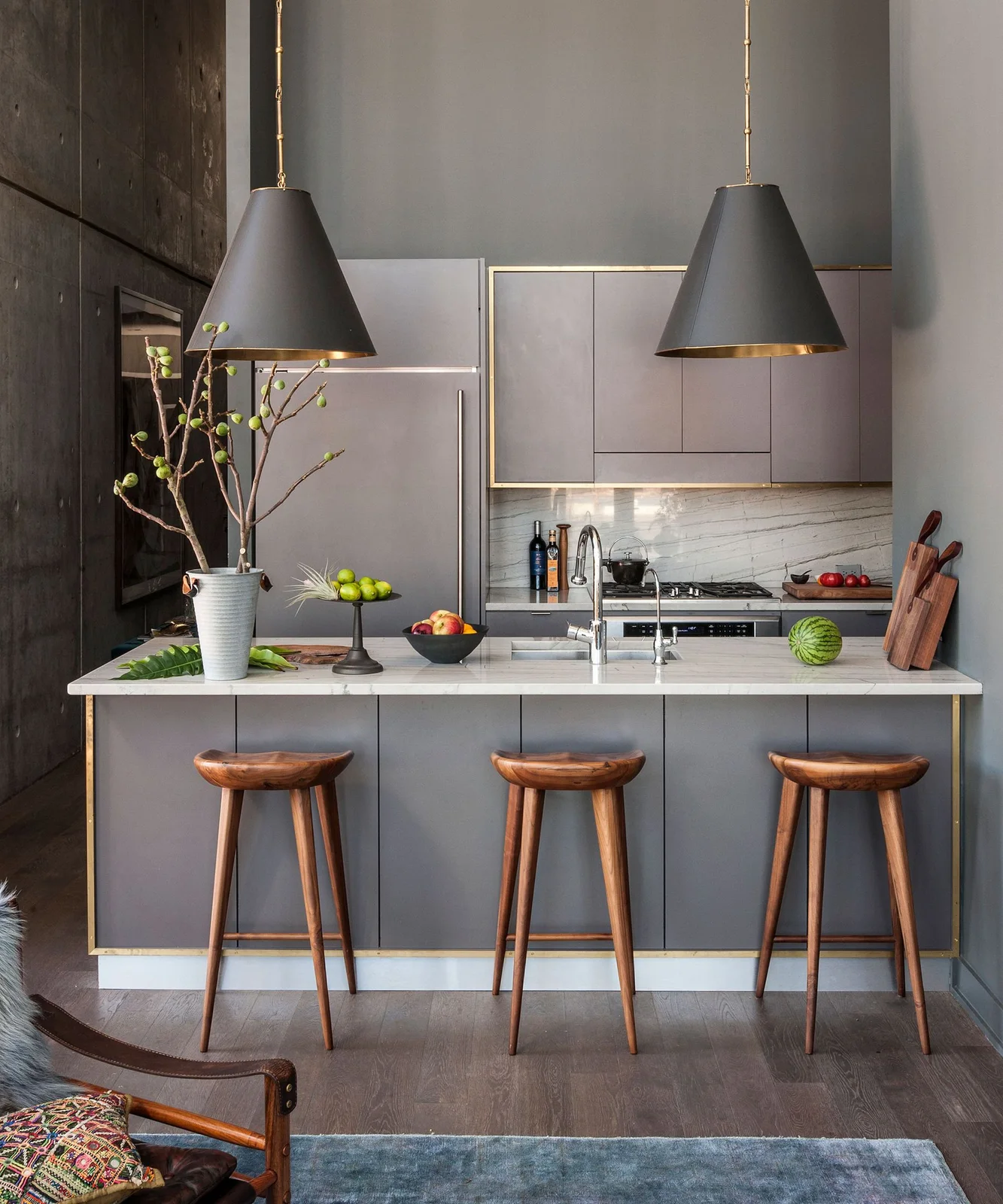 A gray kitchen island and wooden stools sit below dark pendant shades with gold-colored interiors