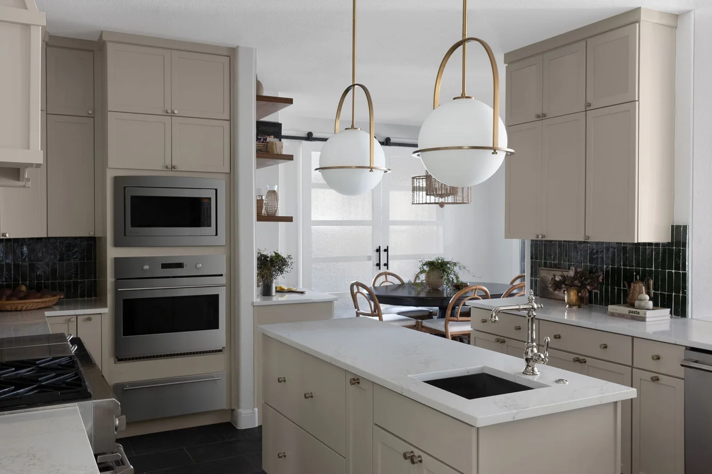 Pale beige kitchen cabinets and a light island sit beside dark green backsplash tiles beneath round white pendant lights