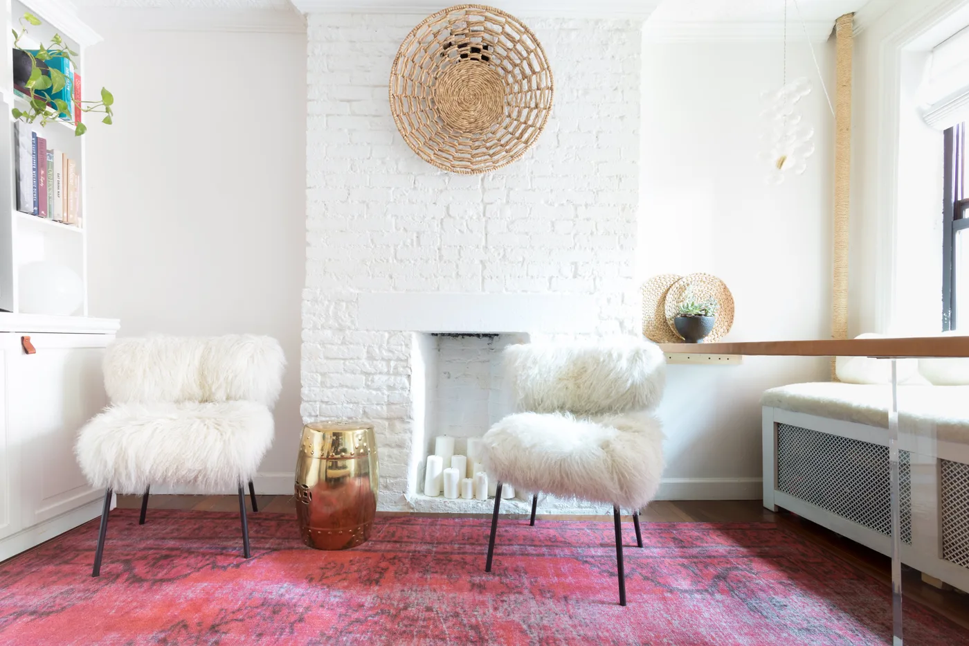 White brick fireplace with pale pillar candles between two fluffy white chairs above a pink rug.