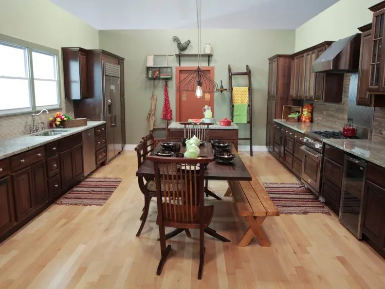 Brown cabinet runs surround a wooden table, bench and chairs beside pale green walls, hanging light, striped rugs and a leaning towel ladder