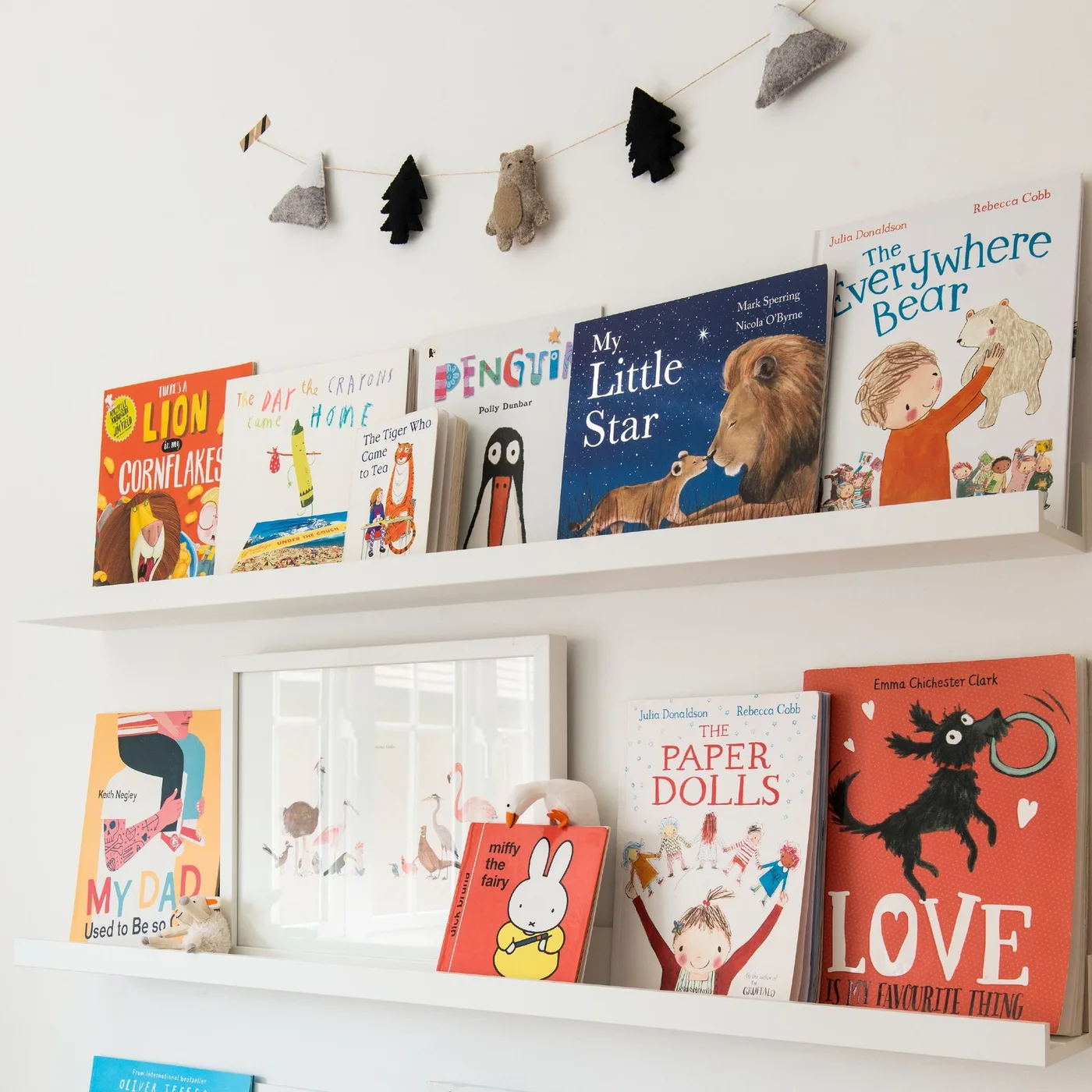 Two narrow white wall ledges hold children’s picture books with their covers facing outward against a plain white wall