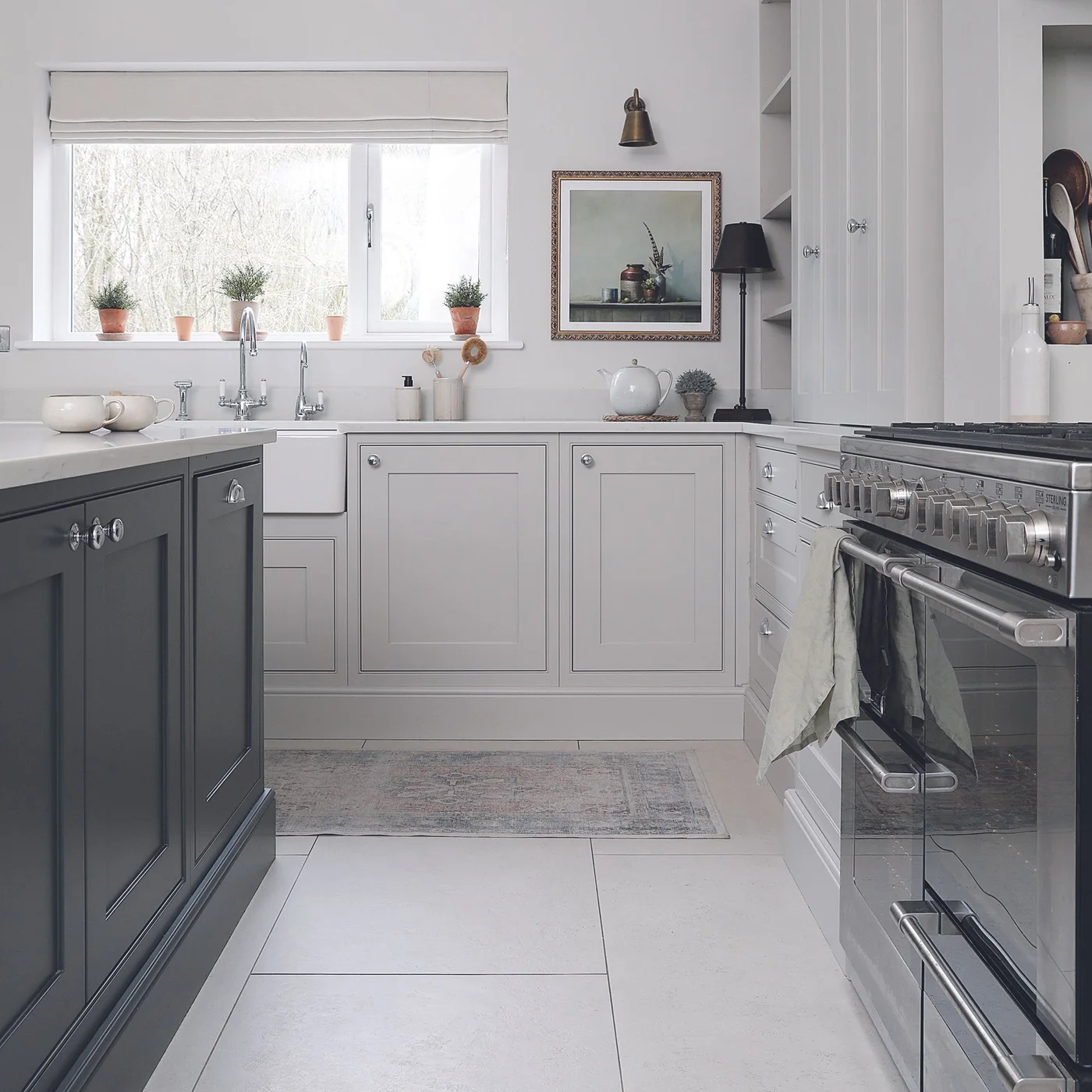 A dark gray island faces paler gray cabinets around a white sink and range cooker in a bright kitchen