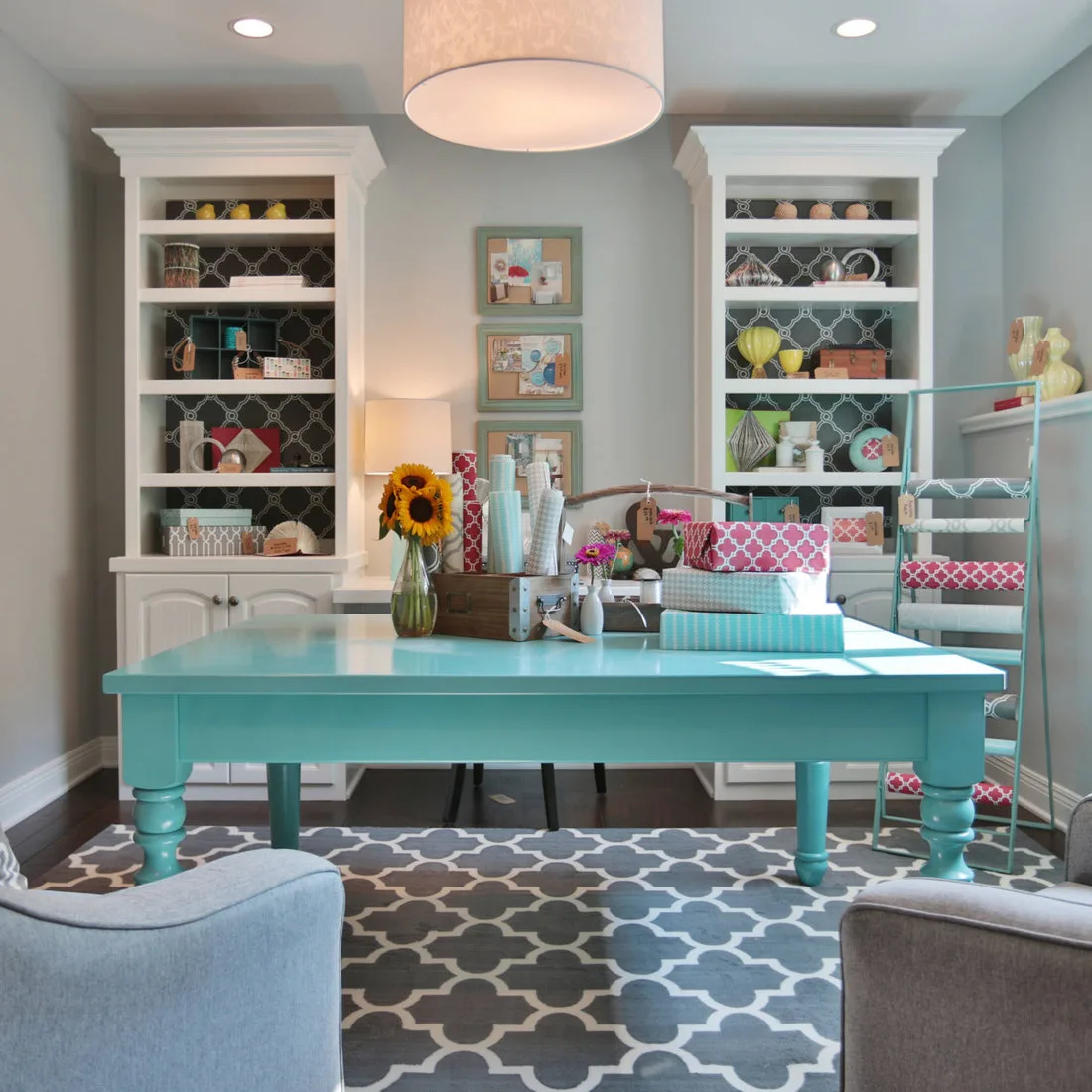Turquoise table beside white built-in shelves, patterned wallpaper, ribbons and craft supplies