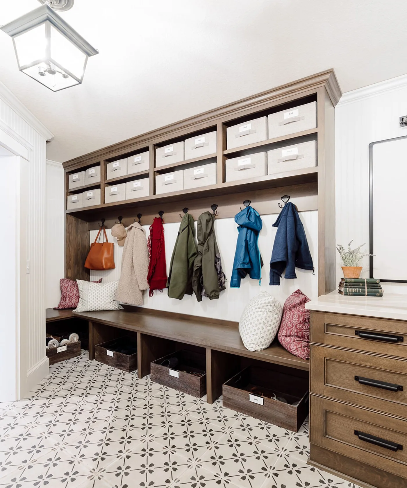 Wood-framed entry storage with upper labeled bins, coat hooks, lower shoe baskets, long bench, side drawers and pale patterned floor