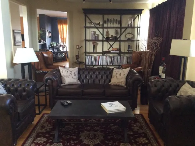 Dark tufted leather sofas surround a low black table with pale cushions, brown leather chairs and open shelving behind them.
